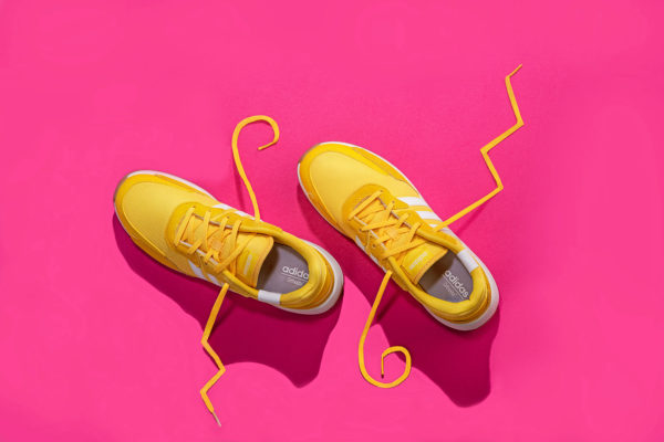 top down photograph of Yellow Adidas tennis shoes on pink background