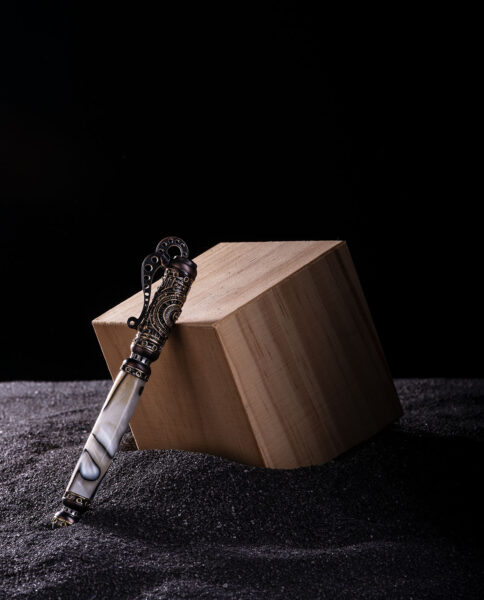 Steampunk Pen leaning against a wooden box surrounded by black sand