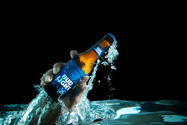 Hand holding a Bud Light Bottle emerging rapidly from a pool of water